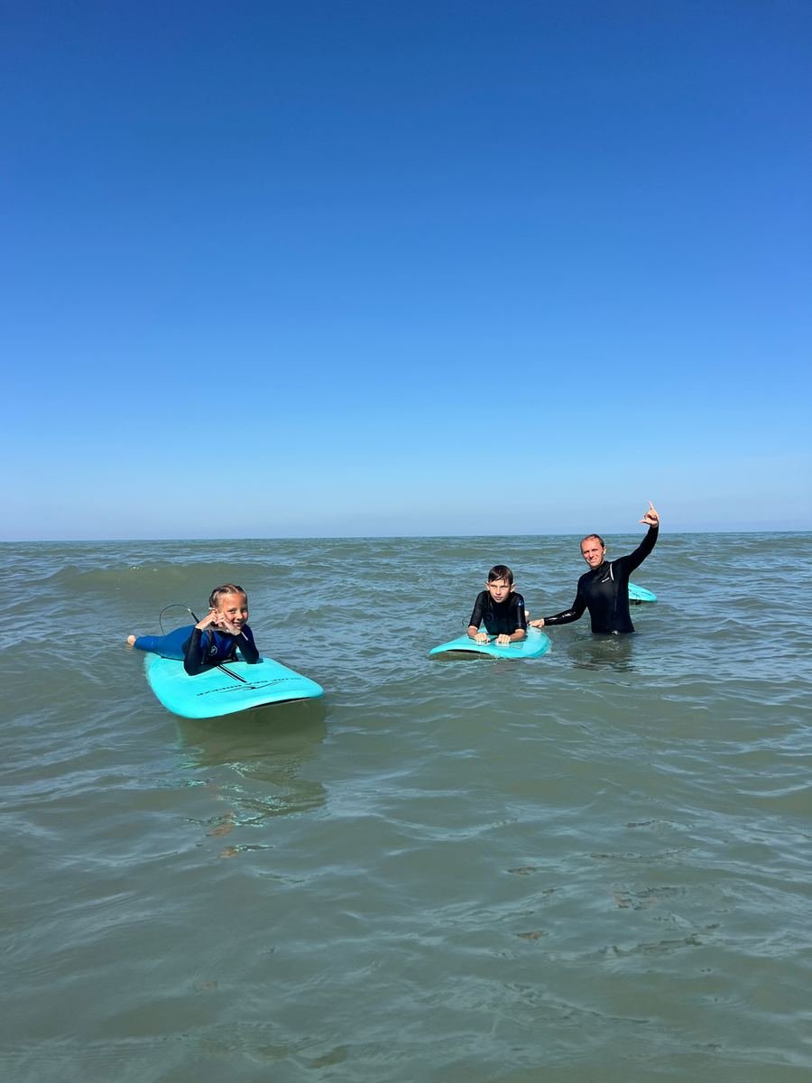 Children on surfboards beside an instructor in the Caspian Sea